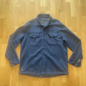 Blå overshirt från Polo Ralph Lauren - Hej, säljer en väldigt schysst overshirt från Polo Ralph Lauren. Skick 7/10, färg marinblå. Storlek L. Passar en som är emellan 180-195. OBS, små defekte, se sista två bilder! Priset går att diskuteras! 