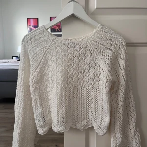 Vit stickad långärmad tröja - Superfin vit stickad tröja med lång ärm och snyggt virkat mönster. Tröjan har en lätt croppad passform och vågig nederkant som ger en trendig look. Perfekt att styla med jeans eller kjol för en chill vibe.