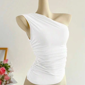 Vit one shoulder topp med rynk - Säljer en vit, tight one shoulder topp med snygga rynkade detaljer i sidorna. Toppens asymmetriska skärning ger en modern vibe och den är gjord i ett stretchigt, mjukt material som sitter skönt mot kroppen. Perfekt för dig som vill sticka ut med en stilren look. Aldrig använd 