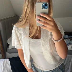 Vit stickad väst med kort ärm - Säljer en vit stickad väst med korta ärmar och öppen front. Västen har en grovstickad struktur som ger en cool och avslappnad vibe. Gullig liten puff arm stil. Klicka gärna på ”köp nu”!