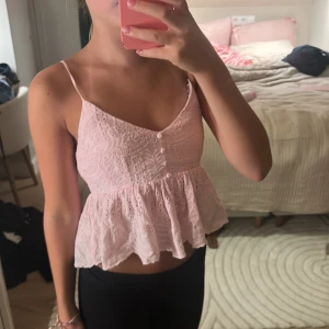 Rosa spetsig blus från Altar'd State - Supersöt ljusrosa blus från Altar'd State med tunna axelband, broderade spetsdetaljer och volang nertill. Toppen har små knappar framtill och en luftig, feminin passform som känns perfekt för varma dagar. Kostar 700 kr i nypris