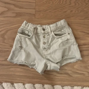 Ljusa jeansshorts med knappar - Snygga ljusa jeansshorts från Zara med hög midja, slitna detaljer och råa kanter. Framtill finns flera silverfärgade knappar och klassiska fickor både fram och bak. Perfekta för sommarens alla äventyr!