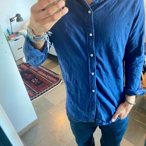 Blå långärmad skjorta med knappar - Snygg blå skjorta med lång ärm och klassisk knappstängning. Skjortan har en avslappnad passform och är tillverkad i ett mjukt bomullstyg. Perfekt för dig som gillar en enkel men stilren look.