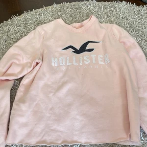 Ljusrosa Hollister sweatshirt S - Säljer en ljusrosa sweatshirt från Hollister i storlek S. Tröjan har ett stort Hollister-tryck och fågel på bröstet, rund hals och långa ärmar. Mjuk insida och klassisk passform, perfekt för chill dagar. Materialet är bomullsmix som känns skönt mot huden.