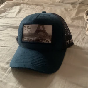 Blå keps från Pianotti med mesh signerad av bille 135 - Snygg blå keps från Pianotti med svart mesh på sidorna och bak. Framsidan har en patch med svartvit bild på Eiffeltornet. Broderad Pianotti-logga på sidan. Justerbar baktill för perfekt passform. Velvet keps pris kan diskuteras