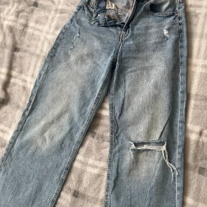 Ljusblå raka jeans från H&M, strl 38 - Ljusblå jeans från H&M i rak modell med hög midja och slitning på ena knät. Klassisk femficksdesign och skön passform. Perfekta till sneakers och en hoodie för en chill look. Liten storlek!