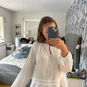 Vit blus med knyt och spetsdetalj - Säljer en luftig vit blus med långa ärmar och rund halsringning med knyt framtill. Blusen har en söt spetsdetalj längs nederkanten och är tillverkad i ett lätt, skrynkligt tyg som ger en chill vibe. Perfekt att styla med jeans eller kjol. Använd en gång