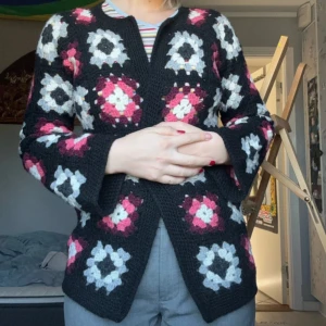 Stickad mormorsrute-kofta i svart och rosa gjord själv  - Unik egenstickad kofta med mormorsrutor i svart, vitt, grått och olika rosa nyanser. Koftan har öppen front och är gjord i ett grovt garn som ger en mysig känsla. Perfekt för dig som gillar retrovibbar och vill sticka ut med färg och mönster.