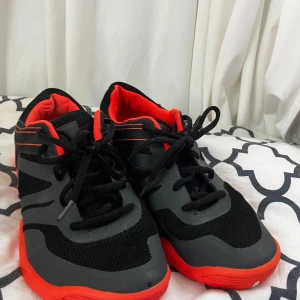 Svarta och orangea sneakers från SOC - Snygga sneakers från SOC i svart och orange med coola detaljer. Ovandelen är i mesh och syntet för bra andningsförmåga och komfort. Skorna har snörning och en platt sula med röd yttersula som sticker ut. Perfekta för dig som gillar sportig stil.