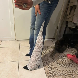 Lågmidjade jeans  - Unika blå jeans med låg midja och raka ben, dekorerade med breda vita spetsinslag längs utsidan av benen. Snygga dragkedjor framtill ger extra edge. Självsydda med symaskin. Strl 29, midjemått 82. Lite urtvättade men annars bra! Fråga om du har några som helst undringar! 🥰