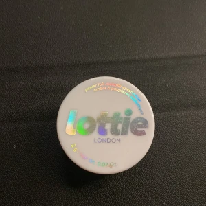 Lottie London Power Foil ögonskugga - Power Foil metallic ögonskugga i färgen 'Unphased' från Lottie London. Kommer i en liten rund burk med holografisk text på locket. Skuggan är intensivt glittrig och har en djup, kopparbrun nyans med metallic finish. Perfekt för att skapa en riktigt bold look. Aldrig använd. Pris kan diskuteras.