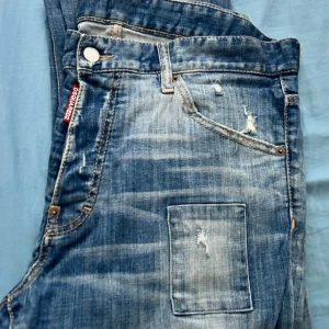 Dsquared2 Cool Guy jeans blå herr - Riktigt snygga Dsquared2 Cool Guy jeans i blå tvätt med slitningar, patchade detaljer och trasiga partier. Klassisk femficksmodell med Dsquared2-logga vid fickan. Jeansen har en modern, avslappnad look och är tillverkade i bomull. MALMÖ!! Pris går att diskutera, Har använt dom 2 gånger 