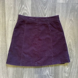 Mörklila manchesterkjol med dragkedja - Snygg mörklila kortkjol i manchester med klassisk A-linjeform, kjolen har en diskret dragkedja bak. Storlek=32 och kjolen är fån H&M. Köpt för många år sen och jag tror den är oanvänd då den är för liten för mig!💕🔮