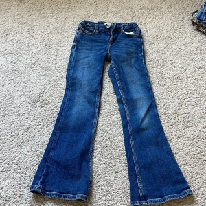 Blå bootcut jeans från Gina Tricot - Snygga blå jeans från Gina Tricot i klassisk bootcut-modell. Jeansen har normal midja, fem fickor och dragkedja med knapp framtill. Tillverkade i jeansmaterial med lätt slitning för en cool look.
