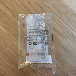 Mix av vita pärlor och silver diamanter  - Säljer ett set med små vita pärlor och silver diamanter, perfekt för att göra egna naglar. Kommer i en praktisk förvaringsask med olika fack för varje typ av pärla och dekoration. Aldrig använt!!! Pris kan diskuteras!