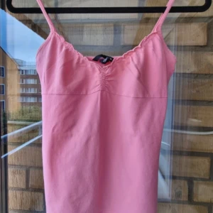 Rosa linnetopp med smala axelband - Snygg rosa linnetopp med smala axelband och lätt rynkdetalj vid bysten. Perfekt för varma dagar och enkel att matcha med jeans eller kjol. Mjuk och skön känsla, passar dig som gillar en feminin och enkel stil.