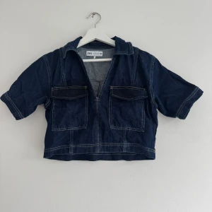 Mörkblå jeanstopp från Zara XS - Säljer denna trendiga jeanstopp från Zara i croppad modell med korta ärmar och två stora bröstfickor. Perfekt för dig som gillar en avslappnad men trendig look.