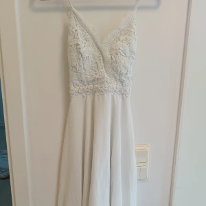 Vit spetsklänning från Chiara Forti - Supersöt vit långklänning från Chiara Forti med blommig spets upptill och omlott-v-ringad urringning. Klänningen har tunna axelband och ett flowy, lätt tyg nedtill. Dragkedja i sidan för enkel påklädning. Perfekt för student eller sommarens alla tillfällen.