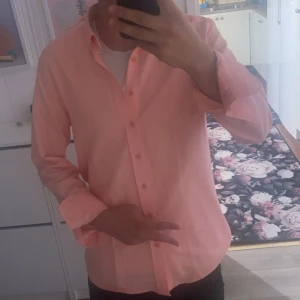 Ljusrosa skjorta från Pierre Cardin - Snygg ljusrosa skjorta från Pierre Cardin med klassisk krage och knappar hela vägen. Skjortan är långärmad och gjord i mjuk bomull, perfekt för dig som gillar stilrena och färgglada plagg. Passformen är normal och skjortan har en clean look.