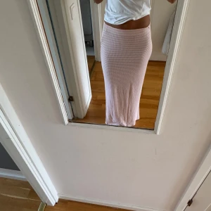 Långrandig rosa kjol med stretch - Säljer en långkjol med smalrandigt mönster i ljusrosa och vitt. Kjolen har en tight passform och är gjord i ett mjukt, stretchigt material som sitter skönt mot kroppen. Perfekt för dig som gillar en enkel men snygg look.