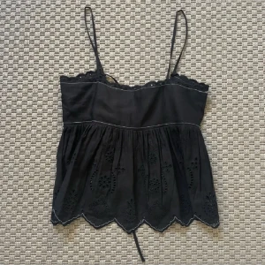 Svart broderad linnetopp från zara - Supersöt svart linnetopp från zara med tunna axelband, broderade blommor och spetsdetaljer längs kanten. Aldrig använd med prislappen kvar. Säljs inte längre