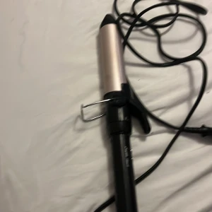 BaByliss Sublim' Touch locktång - Locktång från BaByliss i modellen Sublim' Touch. Den har ett svart handtag med silverfärgade knappar och en cylinder i metallic-rosa. Utrustad med klämma och värmeskyddad topp. Perfekt för att skapa snygga lockar och volym i håret.
