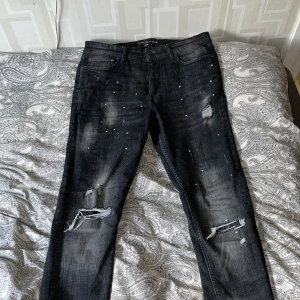 Svarta jeans från supply & demand med slitningar. - Snygga svarta jeans från Supply & Demand med slitna detaljer på knäna och små pärlor framtill. Jeansen har en rak passform och klassisk femficksdesign. Perfekta för dig som gillar en edgy och trendig look.