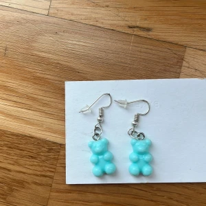 Turkosa björnörhängen i plast - Supergulliga örhängen med turkosa björnar i plast, hängande på silvriga krokar. Perfekt för dig som vill ha en lekfull och färgglad detalj till din look. Björnarna har en 3D-effekt och är riktigt söta, passar dig som gillar unika accessoarer.Jag själv är nickelallergiker och har inte haft några problem. 