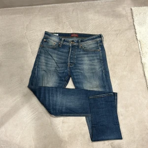 Jack & Jones Tapered Erik jeans blå - Snygga blå jeans från Jack & Jones, modell Tapered/Erik. Jeansen har klassisk femficksdesign, medelblå tvätt och diskreta slitningar för en cool look. Tapered passform som smalnar av nedtill. Tillverkade i bomull med tydliga kontrastsömmar.