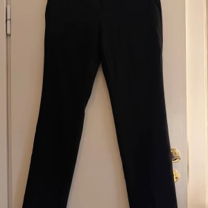 Svarta kostymbyxor Calvin Klein - Snygga svarta kostymbyxor från Calvin Klein med klassisk rak passform. Byxorna har en stilren look och är perfekta för dig som gillar en clean och tidlös stil. Tillverkade i ett mjukt material som känns bekvämt hela dagen.