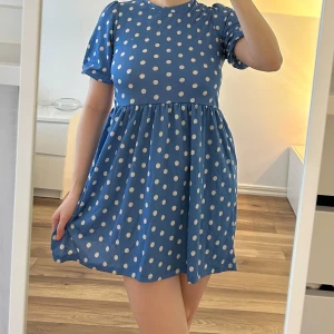 Blå prickig kortklänning med puffärm - Söt blå klänning med vita prickar och puffärmar. Klänningen har rund halsringning och markerad midja. 