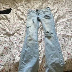 Ljusblå slitna bootcut jeans från H&M - Ljusblå jeans med bootcut passform från H&M. Jeansen har slitna detaljer och hål på låret och knät, klassiska fem fickor och stängs med dragkedja och knapp. Midja rakt över 14cm men det går att justera själv på jeansen, innerlår 30cm, lågmidjade 5cm