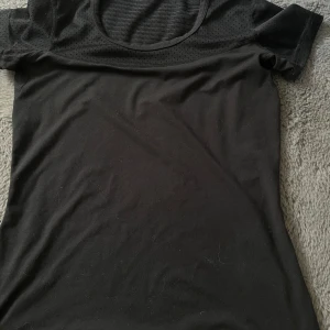 Svart tränings t-shirt - Svart t-shirt med meshdetaljer upptill och på ryggen. T-shirten har rund halsringning och korta ärmar. Perfekt för träning eller en sportig look. Passar både XS & S.