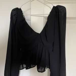 Svart blus med volang från H&M - Säljer en svart blus från H&M med långa, luftiga ärmar och volang nertill. 