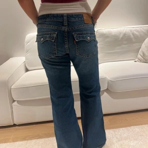 Blå bootcut jeans från Levi's - Snygga blå bootcut jeans från Levi's med klassiska bakfickor och bruna detaljer vid linningen. Jeansen har en normal passform och är perfekta för en avslappnad stil. Passar dig som gillar tidlös denim med lite utsvängda ben.