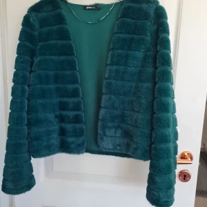Grön pälsjacka från Gina Tricot - Säljer en fluffig och mjuk grön pälsjacka från Gina Tricot. Jackan har lång ärm, horisontella sömmar och öppen front utan knäppning. Perfekt för dig som vill sticka ut med en färgglad och trendig look.