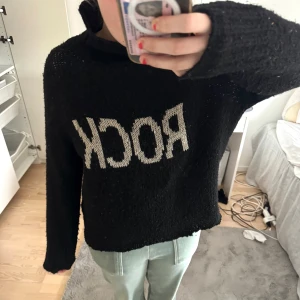 Svart stickad polotröja med texten ROCK - Svart stickad polotröja med vit text 'ROCK' framtill. Tröjan har en oversized passform och långa ärmar. Perfekt för dig som vill ha en cool och avslappnad stil. Storlek M och bra skick! Nypris 899kr💕