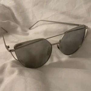 Silvriga pilotbågar solglasögon - Snygga solglasögon med pilotbågar i silverfärgad metall och mörka linser. Ramen har en modern design med dubbla bryggor och tunna skalmar. Perfekt accessoar för en cool look.