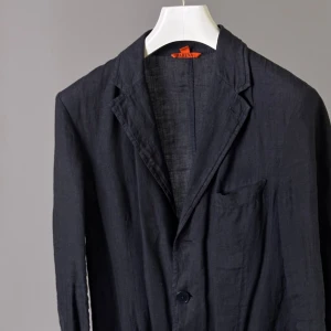 Navy linne kavaj från Barena - Stilren mörkblå kavaj från Barena i ett lätt och luftigt linnematerial. Klassisk design med smal krage, enkelknäppning och bröstficka. Perfekt för dig som vill ha en avslappnad men ändå dressad look.