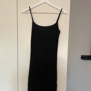 Svart ribbad långklänning från Amisu - Säljer en svart ribbad långklänning som går till smalbenen från Amisu med smala axelband och rundad halsringning. Klänningen har en tight passform och är perfekt för dig som gillar en enkel och stilren look. Den har även en slits på ena benet vilken gör den superfin!❤️pris kan diskuteras!
