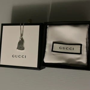 Gucci ghost halsband  - Unikt halsband från Gucci i silverfärg med ett spökhänge dekorerat med GG-loggor. Kedjan är tunn och smidig, perfekt för dig som gillar statement-smycken med en lekfull twist. Halsbandet är silver och samma med Gucci spöket