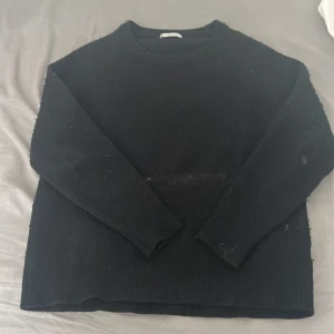 Svart stickad tröja - En enkel svart stickad tröja med rund halsringning och långa ärmar. Tröjan har ribbade muddar vid ärmslut och nederkant, vilket ger en klassisk och stilren look. Perfekt för lager-på-lager under kyligare dagar. Storlek xl men krympt så den är som storlek s