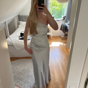 Balklänning/brudtärneklänning från Six Stories - Balklänning/brudtärneklänning från märket ”Six Stories”. Den tidigare ägaren har klippt av lappen i ryggen då den skavde.  Klänningen är i fint skick, möjligtvis med några små tecken på användning. Den är i storlek 40, men passar mig som brukar ha 36/38. Den går säkert att sy in också till önskad passform! Klänningen går i färgerna silver, grå och is blå  Klänning är väldigt lång och går ner till marken på mig som är ca 179cm lång, så den är helt perfekt för långa personer!