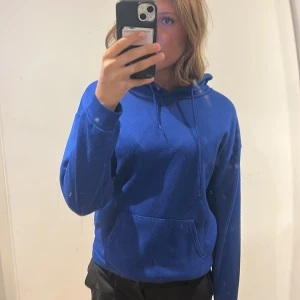 Blå hoodie med ficka - Säljer en klassisk blå hoodie med huva och dragsko. Tröjan har en stor magficka framtill och långa ärmar. Perfekt för en avslappnad stil och enkel att matcha med det mesta.