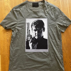 Grön t-shirt  från Limitato - Snygg grön t-shirt från Limitato med ett stort svartvitt fototryck på bröstet. Motivet föreställer en man med pistol, inspirerat av James Bond. Perfekt för dig som gillar unika prints och laidback