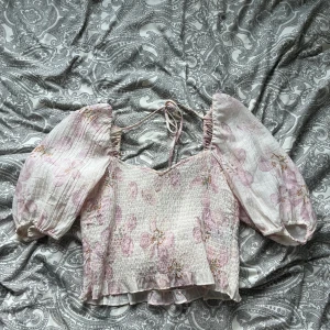 Blommig offshoulder blus med puffärmar - Söt blommig blus i ljusrosa och vit med stora puffärmar. Smockad överdel och liten volang nertill, samt knytband i ryggen. Skriv för frågor💕