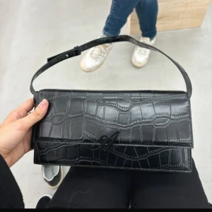 Svart axelväska i krokopräglat skinn från Axel Arigato - Säljer en svart axelväska från Axel Arigato i krokopräglat skinn. Nypris 2150 kr, Dustbag och förpackning medföljer! Har även kvar digitalt bevis på att den är köpt i axelarigatos butik. Självklart äkta! Pris kan diskuteras vid snabb affär! 