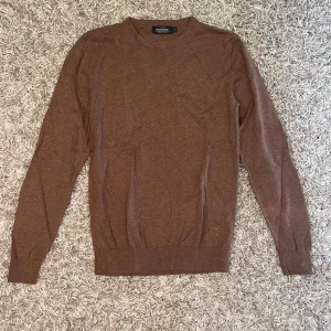 Brun stickad tröja  - Säljer en klassisk brun stickad tröja. Tröjan har rund halsringning och långa ärmar, perfekt för lager-på-lager. Enkel och stilren design som passar till mycket.