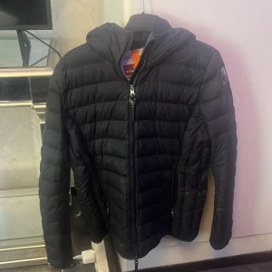 Svart dunjacka från Parajumpers - Säljer en svart dunjacka från Parajumpers i storlek L. Jag som bär S så passar denna jackan perfekt på, den är liten i storleken så skulle säga att den är S. ( L är barnstorleken )  Jackan är superlätt, har huva och dragkedja framtill. Klassisk quiltad design med märkets logga på ärmen. Perfekt för kyliga dagar när du vill ha något både snyggt och funktionellt. Lite små slitig fram vid armen och på sidan med ett litet hål ( skriv för att få se mer bilder ) ändå så är den bra skick. 