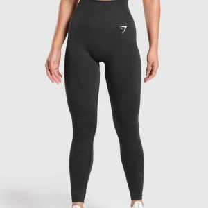 Mörkgrå seamless tights från Gymshark - Mörkgrå tights med hög midja från Gymshark. De är sömlösa och har diskreta mönster längs benen för en sportig look. Perfekta för träning och sitter tight mot kroppen. Liten vit logga framtill vid höften.